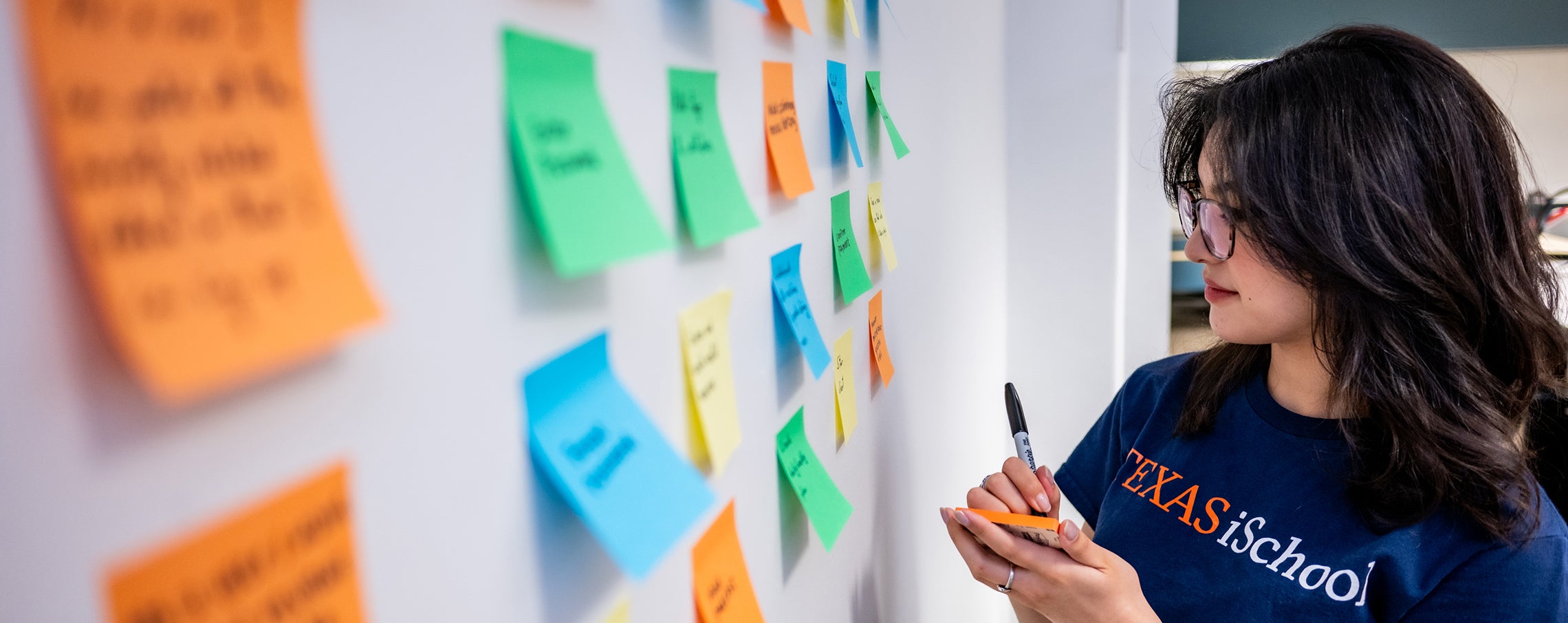 iSchool undergraduate student looking at wall with sticky notes 