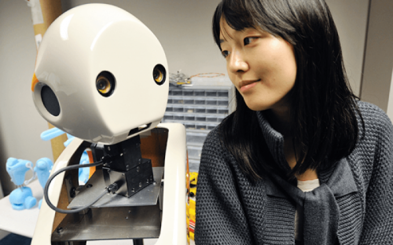 A picture of Dr.Min Kyung Lee sitting next to a robot