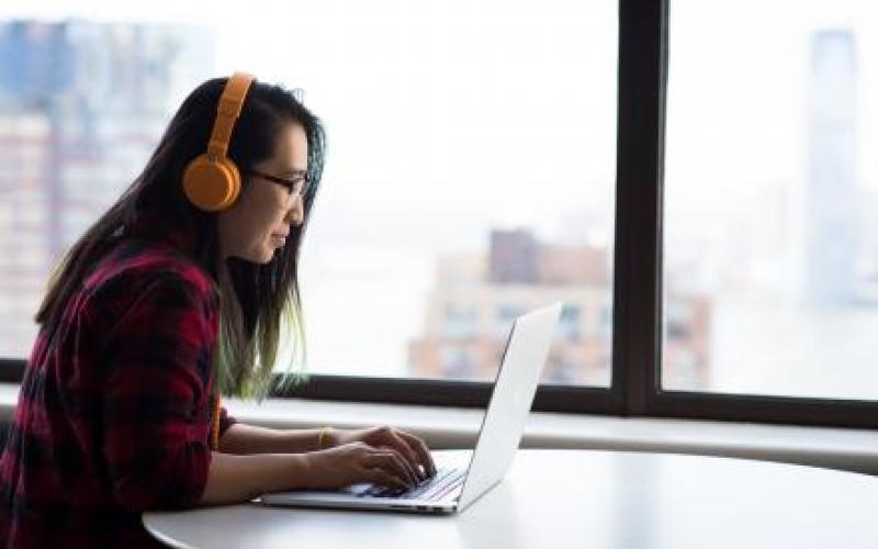 Female student with orange headphones working on laptop